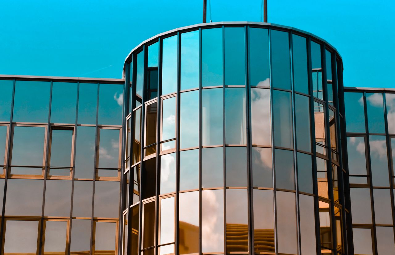 Économiser de l’argent grâce à la pose de films solaire ! A contemporary building with glass panels reflecting a clear blue sky, showcasing modern architecture.
